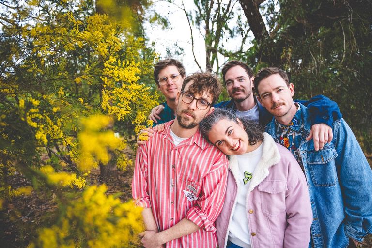 Australian indie rock group Ball Park Music posing together outdoors next to yellow wattle blossoms.
